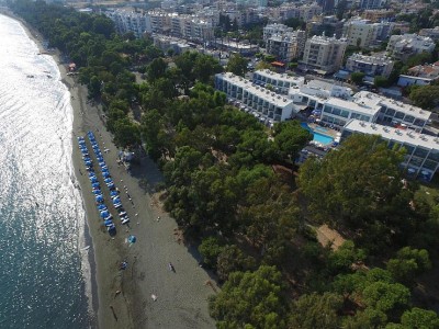 Luftaufnahme eines Strandhotels mit Reihen blauer Sonnenschirme und üppigen Bäumen entlang der Küste