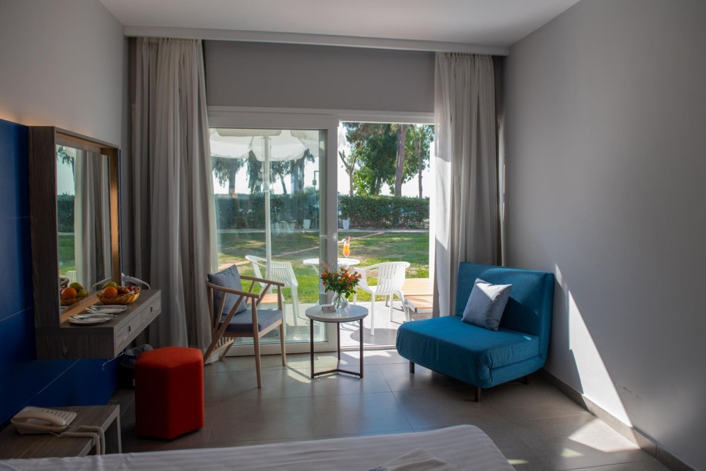 Helles Hotelzimmer mit blauen und grauen Möbeln, Terrassenblick auf einen grünen Garten und kleinem Sitzbereich im Freien