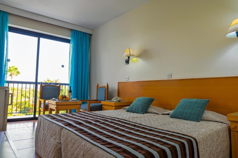 Gästezimmer mit Doppelbett, Balkon, Stuhl und Tisch am Fenster.
