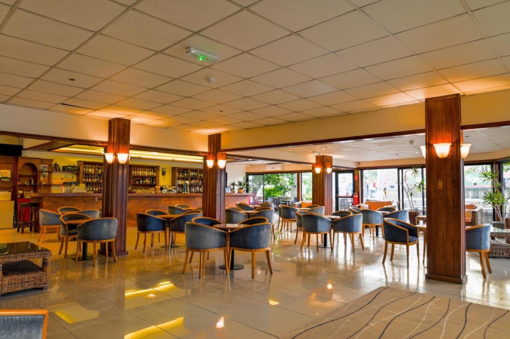 Hotellounge mit Bar, Sesseln, Holzsäulen und großen Fenstern.