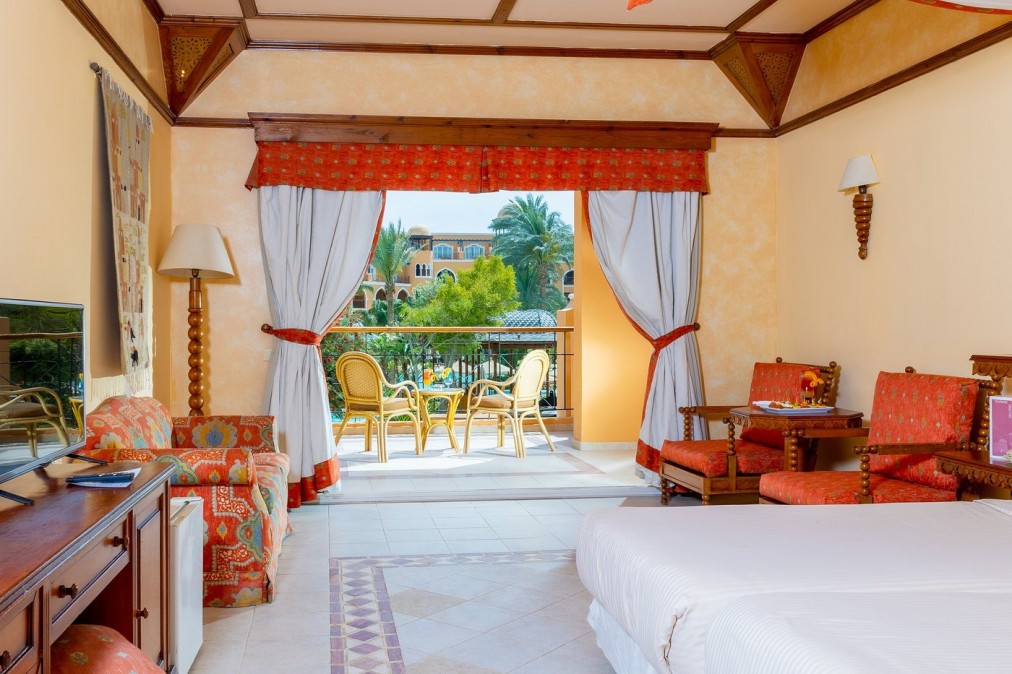 Hotelzimmer mit Doppelbett, roter Einrichtung und Balkon mit Gartenblick