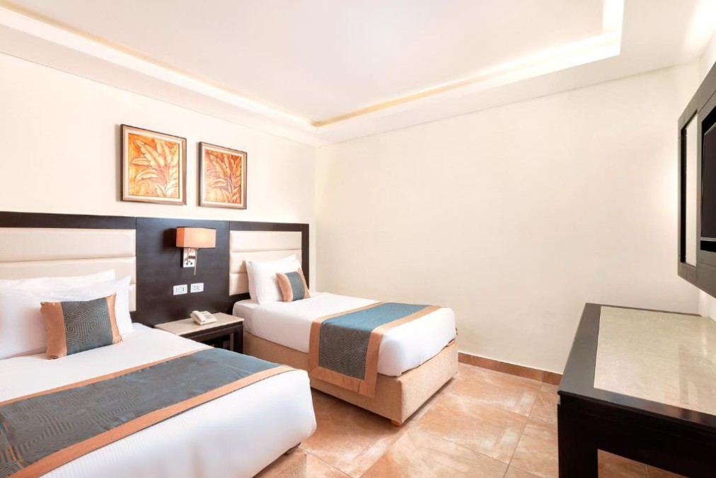 Helles Hotelzimmer mit zwei Einzelbetten, Wandkunst, Fernseher und neutraler Einrichtung