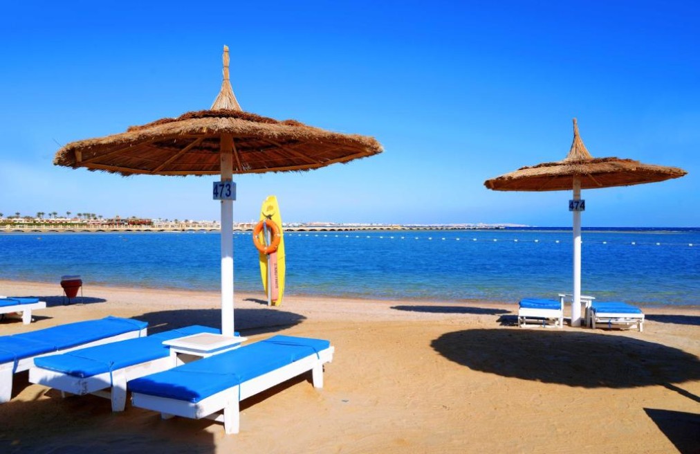 Sandstrand mit blauen Liegen und Strohschirmen mit Blick auf das Meer