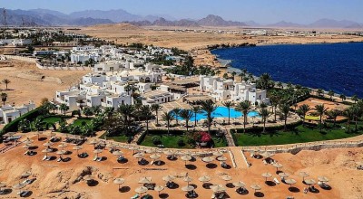 Luftaufnahme eines Ferienresorts am Meer mit weißen Gebäuden, Palmen, Pools und Sonnenliegen mit Blick auf das Rote Meer