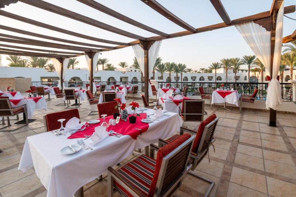 Offene Restaurantterrasse mit rot-weißen Tischdekorationen und Blick auf Palmen und Resortgebäude