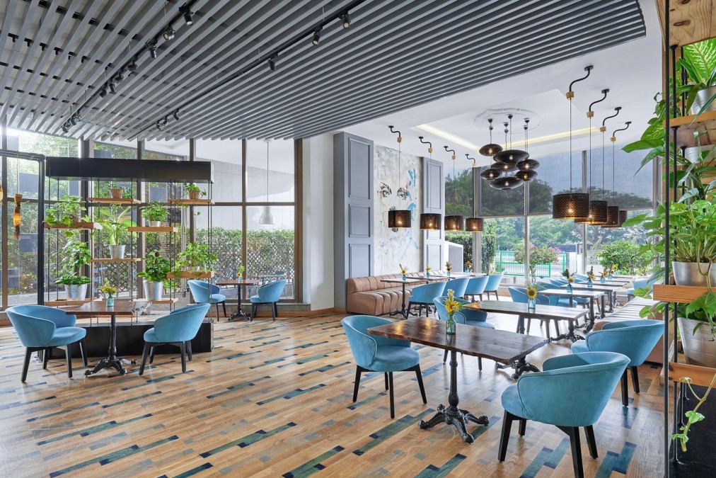 Moderne Hotellounge mit türkisfarbenen Stühlen, Pendelleuchten, Pflanzen und Tischen – Bereich zur Erholung im Trainingslager