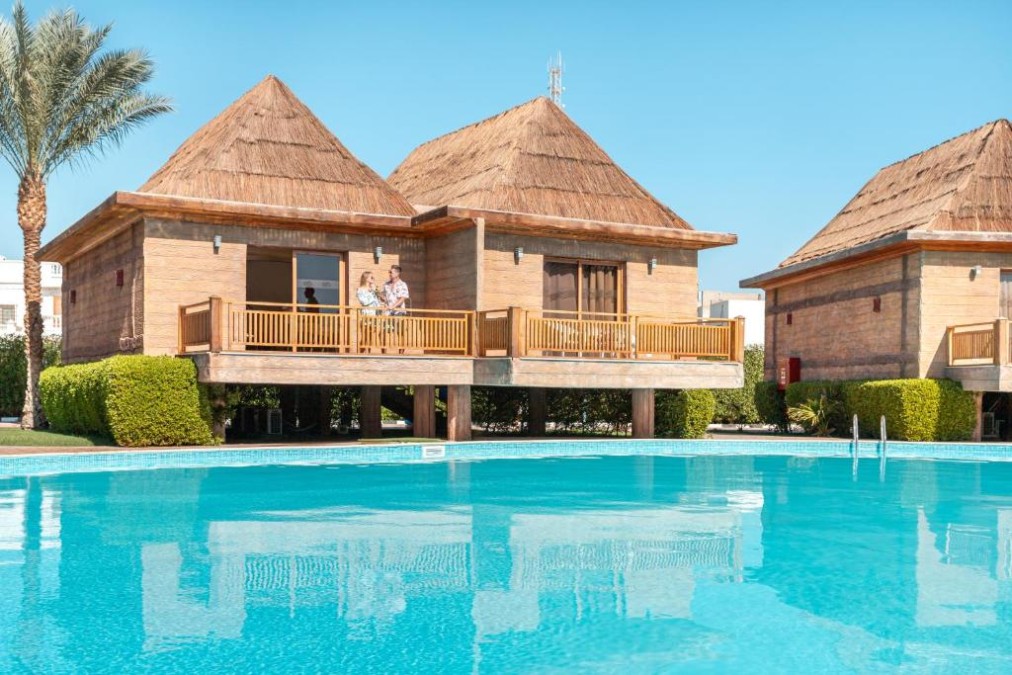 Bungalows am Pool auf Stelzen mit Reetdächern neben einem großen Außenpool.