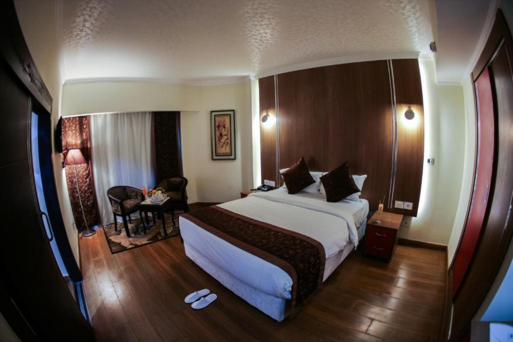 Doppelzimmer mit Bett, kleinem Tisch mit Stühlen und bodenlangen Vorhängen.
