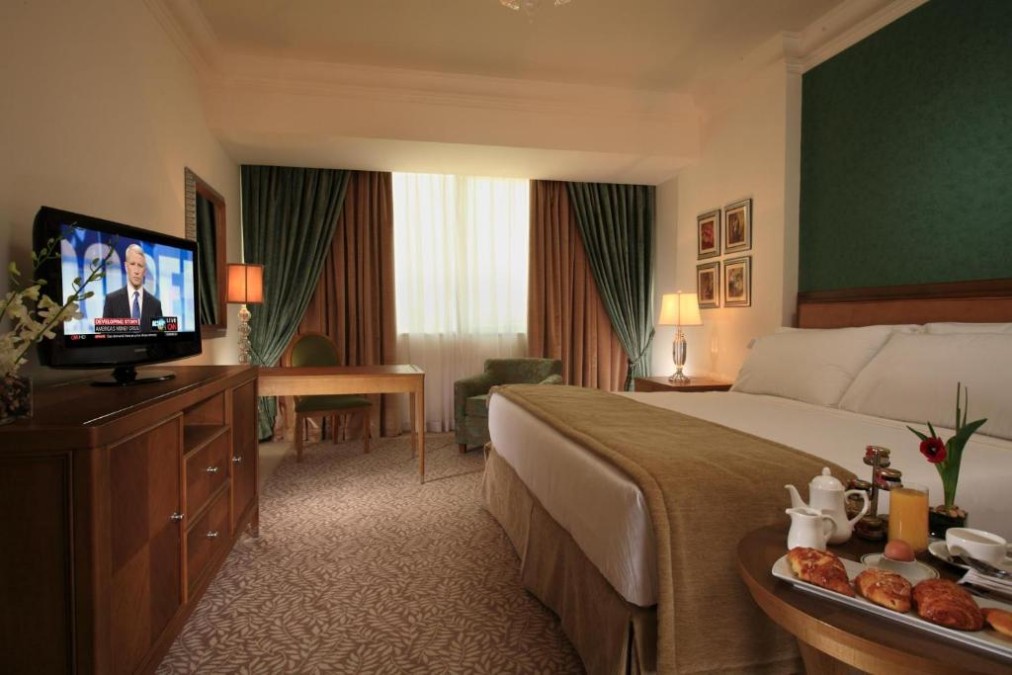 Zimmer mit Kingsize-Bett, Schreibtisch, TV, Sessel und Frühstückstablett auf einem Beistelltisch.