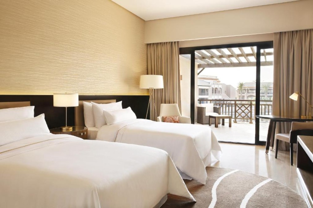 Twin-Zimmer mit zwei Betten, Schreibtisch und Schiebetüren zum Balkon mit Blick auf das Resort.