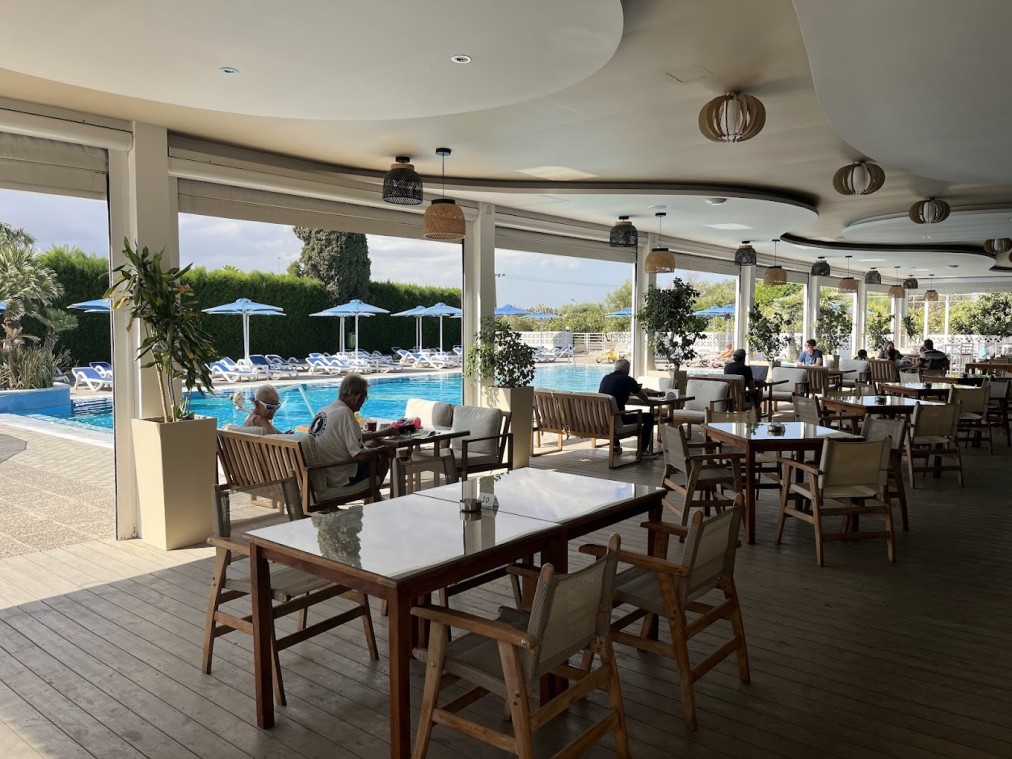 Überdachte Restaurantterrasse am Außenpool mit Tischen und sitzenden Gästen.