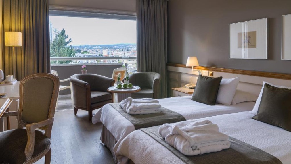 Zweibettzimmer mit Balkonblick, Schreibtisch und Sesseln.