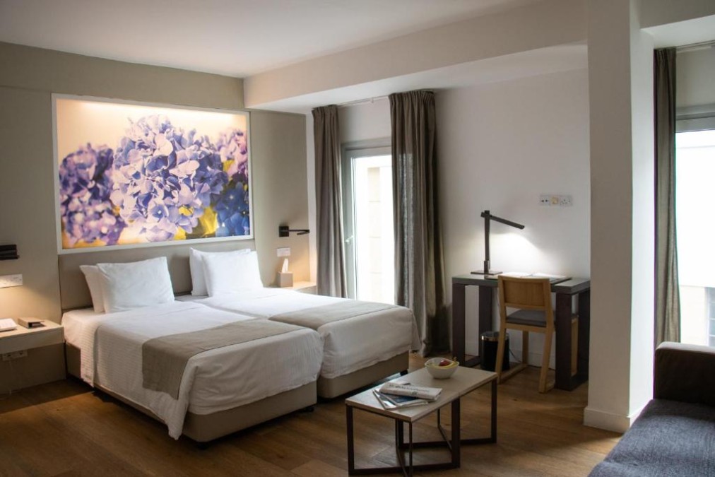 Helles Gästezimmer mit zwei Betten, Schreibtisch, Sofa und großem Blumenwandbild.