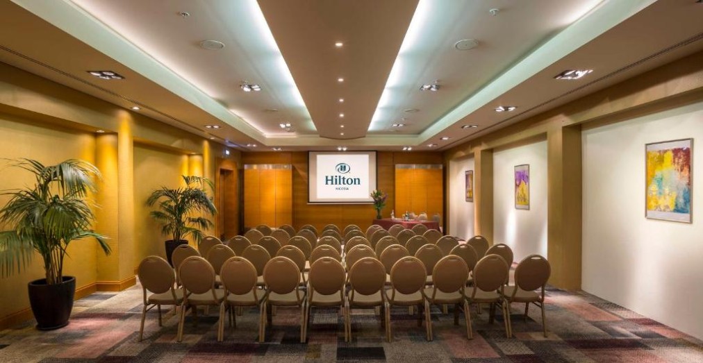 Konferenzraum mit Reihenbestuhlung und Präsentationsbildschirm.