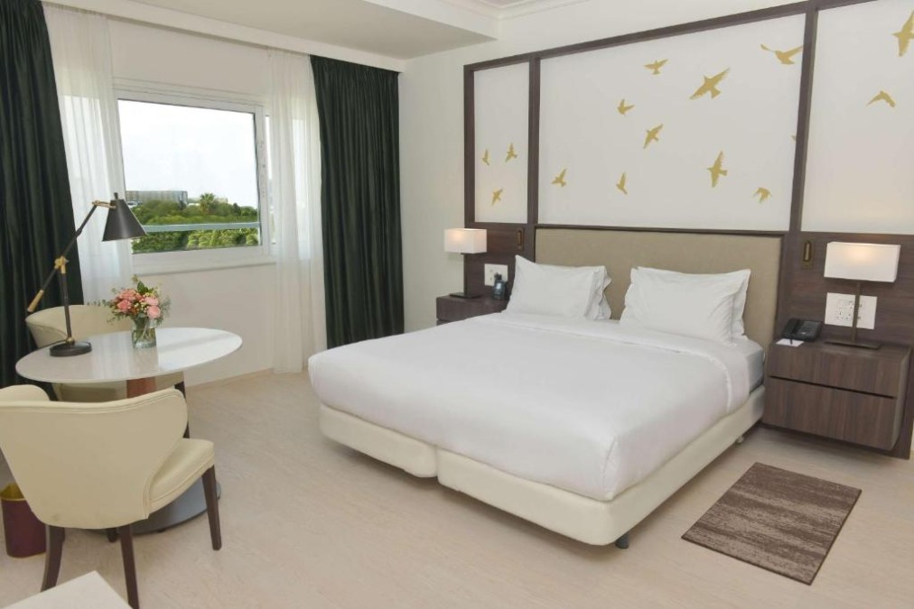 Zimmer mit Kingsize-Bett, Schreibtisch, Sessel und großem Fenster.