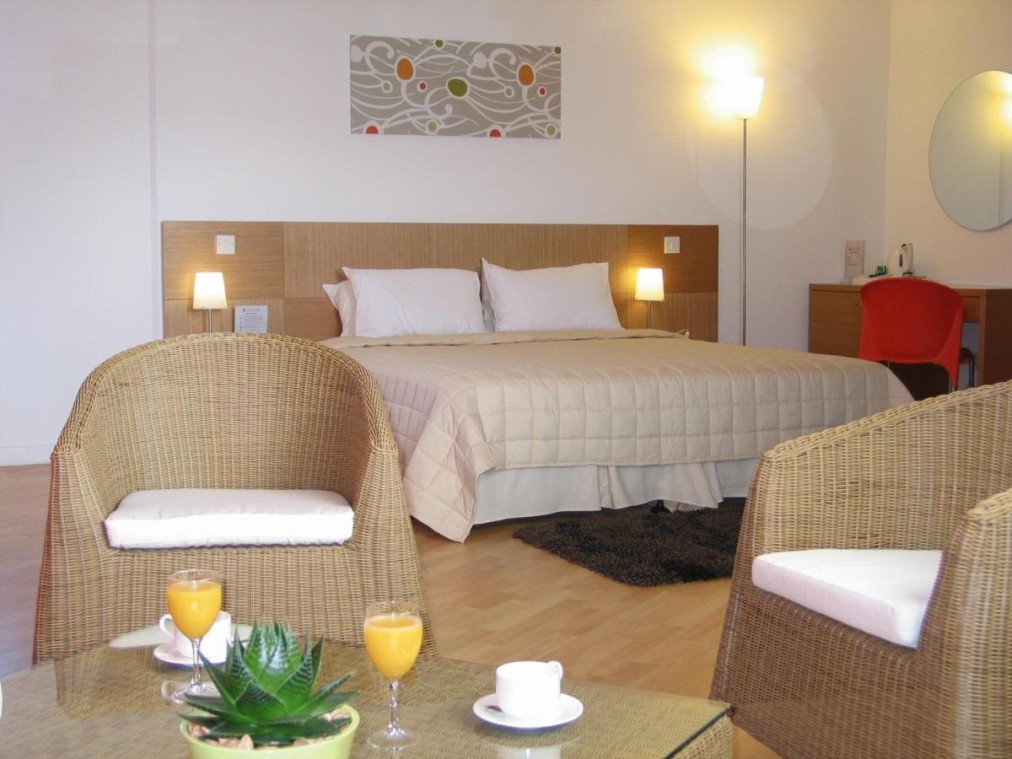 Chambre d'hôtel spacieuse avec lit double, fauteuils en rotin et table basse avec jus d'orange