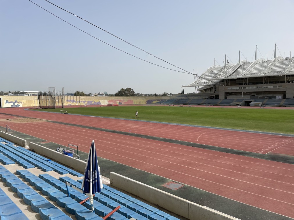 Stade d'athlétisme avec piste de course rouge, terrain vert et tribune moderne utilisé pour les stages d'entraînement et séances d'entraînement