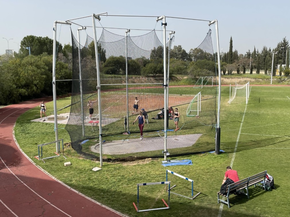 Athlètes pratiquant le lancer du disque ou du marteau à l'intérieur d'une cage filetée sur terrain d'entraînement herbeux