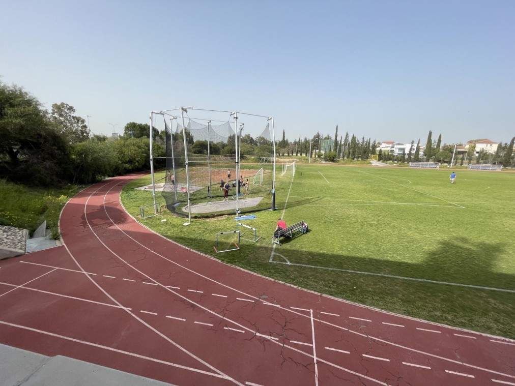 Terrain d'athlétisme avec cage de lancer, couloirs de piste et zone d'entraînement verte pour exercices d'épreuves de terrain