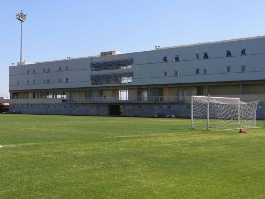 Terrain d'entraînement de football vert avec cage de but et bâtiment sportif moderne à plusieurs niveaux