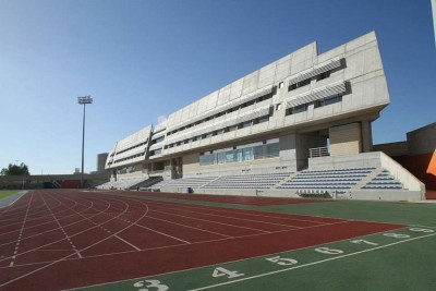 Stade d'athlétisme moderne avec piste de course rouge et grande tribune sous un ciel bleu dégagé