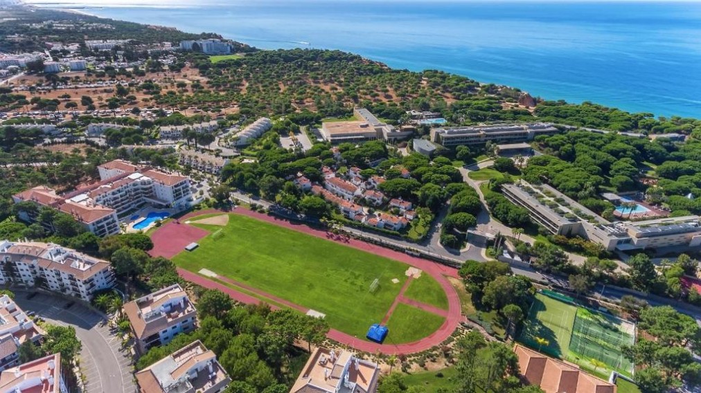 Vue aérienne d'ensemble d'un complexe sportif côtier avec piste d'athlétisme, terrains et courts.