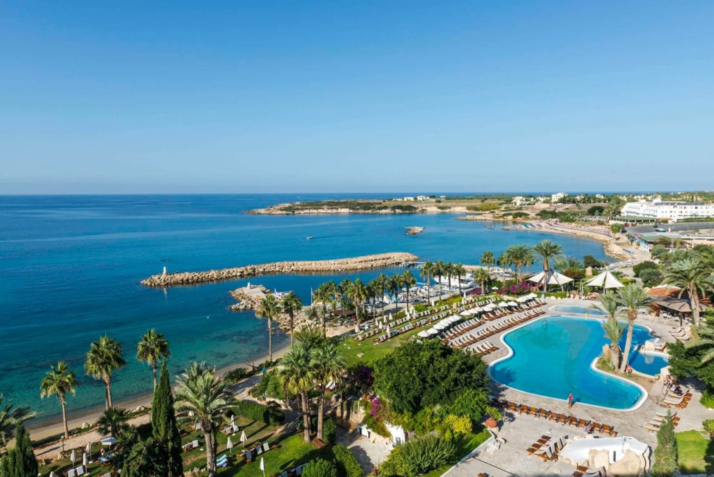 Vue aérienne d'un complexe en bord de mer avec grande piscine extérieure et transats face à la mer