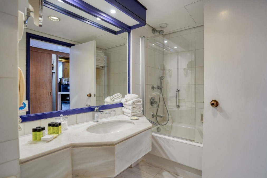 Salle de bain avec carrelage blanc, baignoire et comptoir avec articles de toilette et serviettes pliées