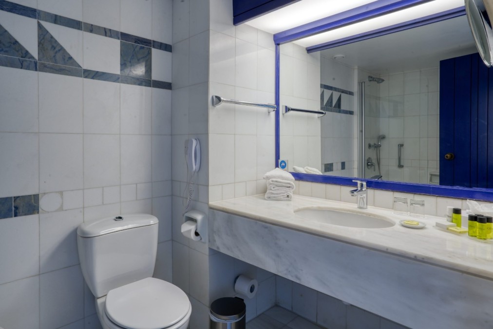 Salle de bain carrelée de blanc avec miroir, lavabo et équipements modernes préparés pour les clients