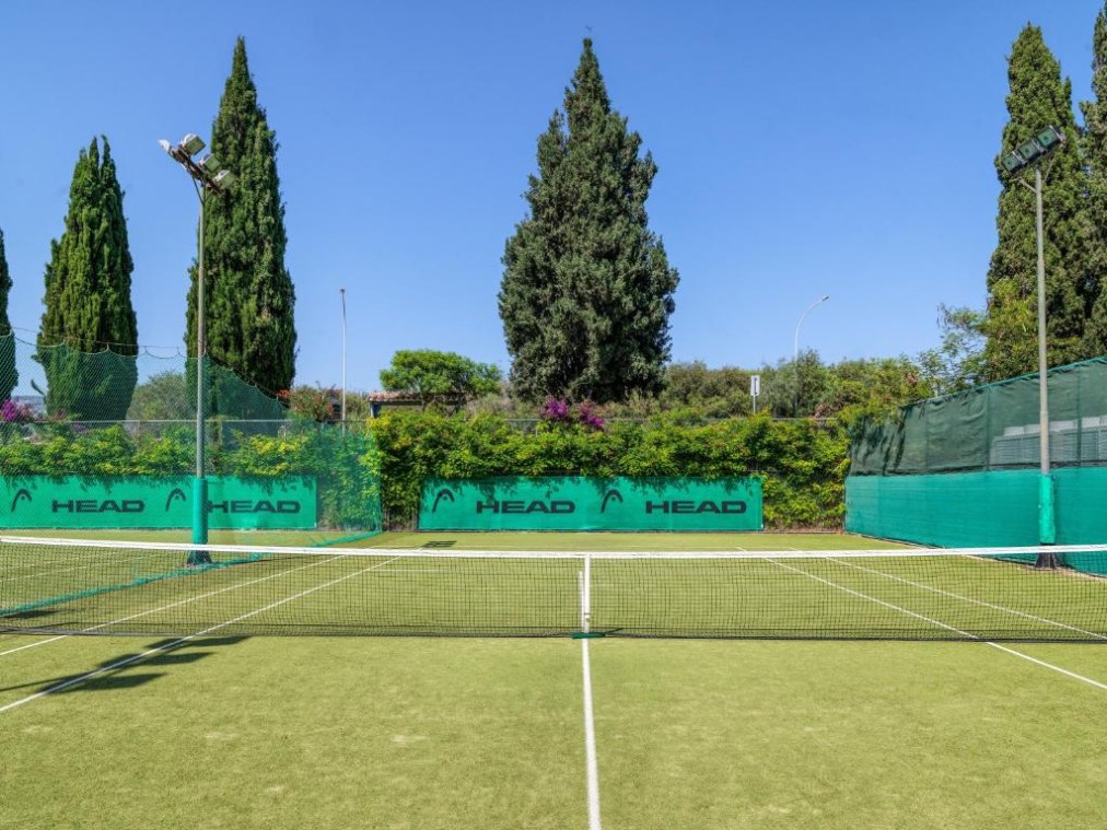 Court de tennis extérieur avec surface verte, entouré de grands arbres et filets verts de marque HEAD pour les séances d'entraînement