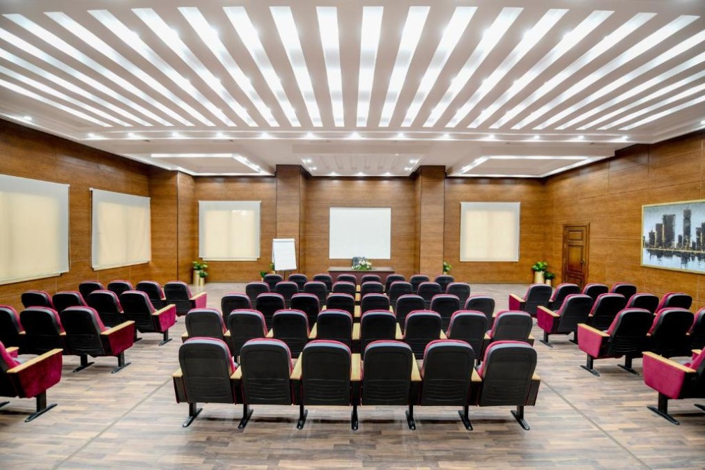 Salle de conférence avec rangées de chaises rouges face à un écran de projection