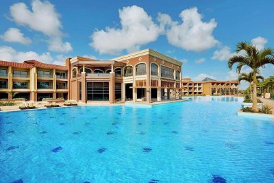 Grande piscine du complexe devant les bâtiments de l'hôtel sous un ciel bleu.