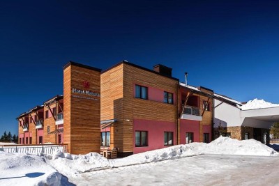 Extérieur de l'hôtel enneigé avec bardage en bois sous un ciel d'hiver dégagé.