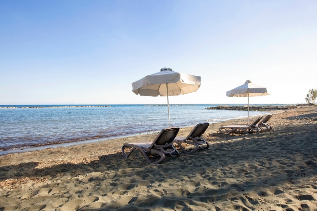 Plage de sable avec chaises longues et parasols blancs près d'une eau de mer calme