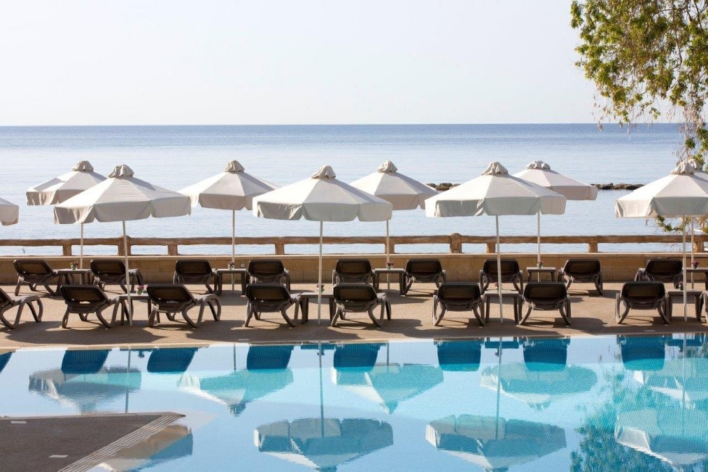 Vue au bord de la piscine avec rangées de chaises longues et parasols blancs donnant sur la mer bleue calme