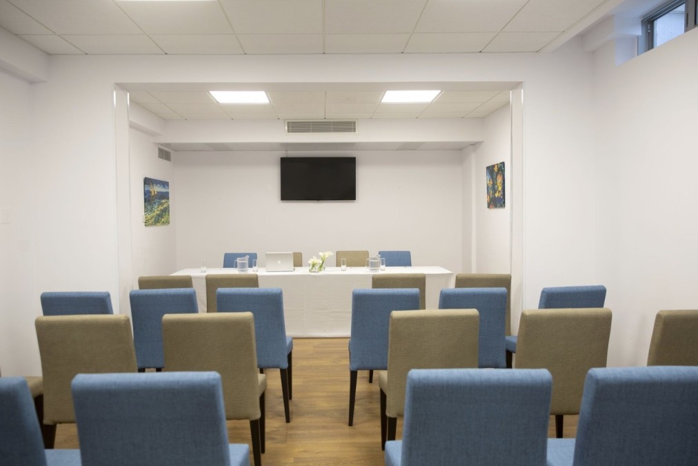 Petite salle de conférence avec rangées de chaises face à une table et un écran mural