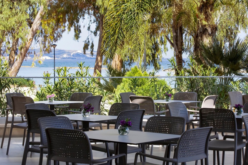Espace restauration extérieur entouré de verdure avec tables donnant sur la mer