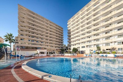 Piscine extérieure avec solarium environnant et bâtiments à plusieurs étages.