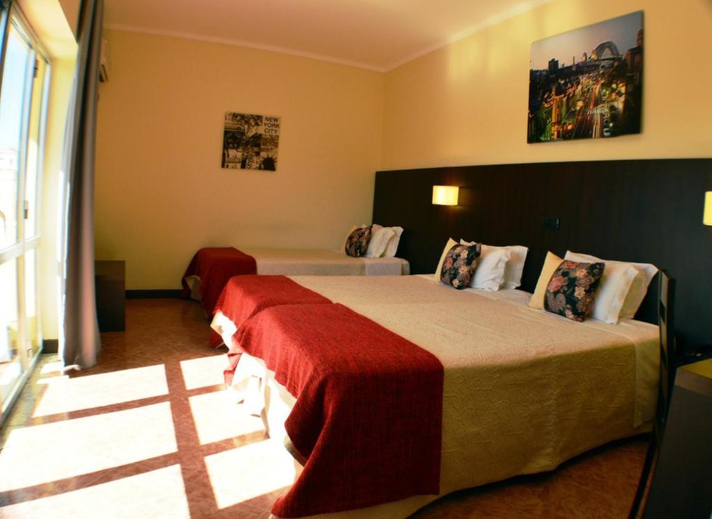 Chambre triple avec trois lits simples et lumière naturelle depuis les portes-fenêtres du balcon.