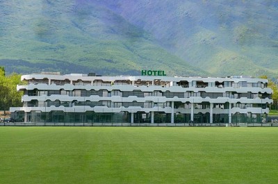 Bâtiment d'hôtel face à un terrain de football verdoyant avec montagnes en arrière-plan, hébergement pour stage sportif