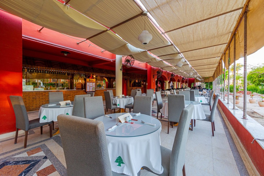 Terrasse de restaurant extérieure avec tables rondes, nappes blanches et toit en auvent