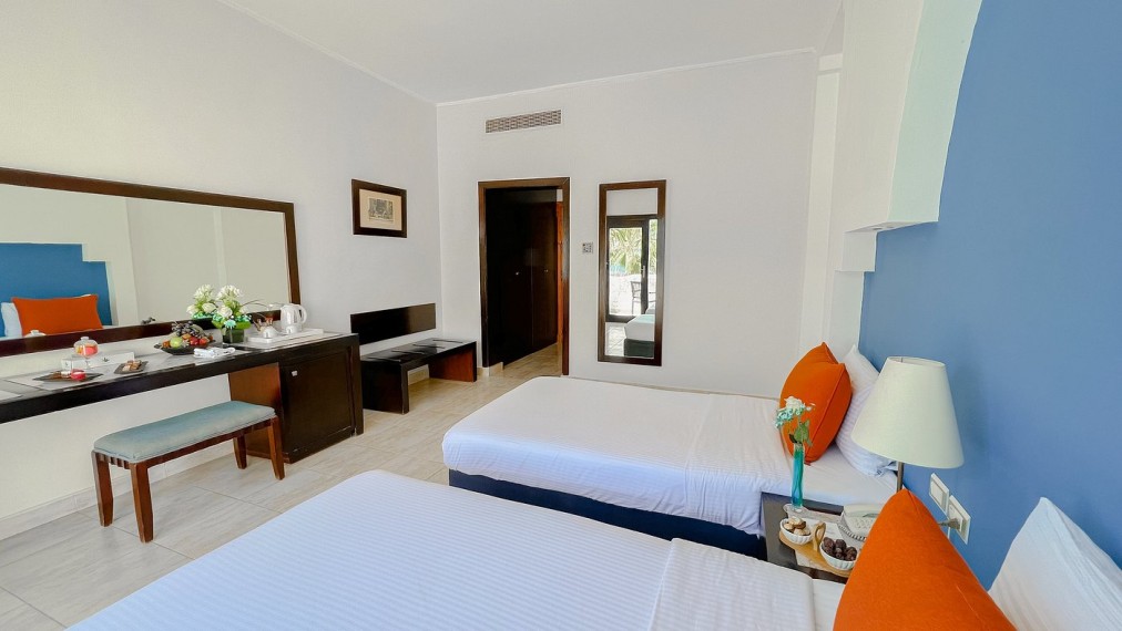 Chambre d'hôtel moderne avec lits jumeaux, mur d'accent bleu et oreillers orange, comprenant un bureau de travail et une décoration fraîche