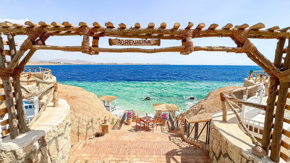 Escalier en bois menant aux cabanes de plage et à la mer turquoise sous une enseigne indiquant 