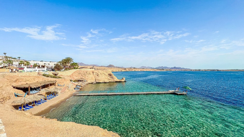 Baie turquoise cristalline avec transats, parasols en chaume et jetée en bois s'avançant dans la mer