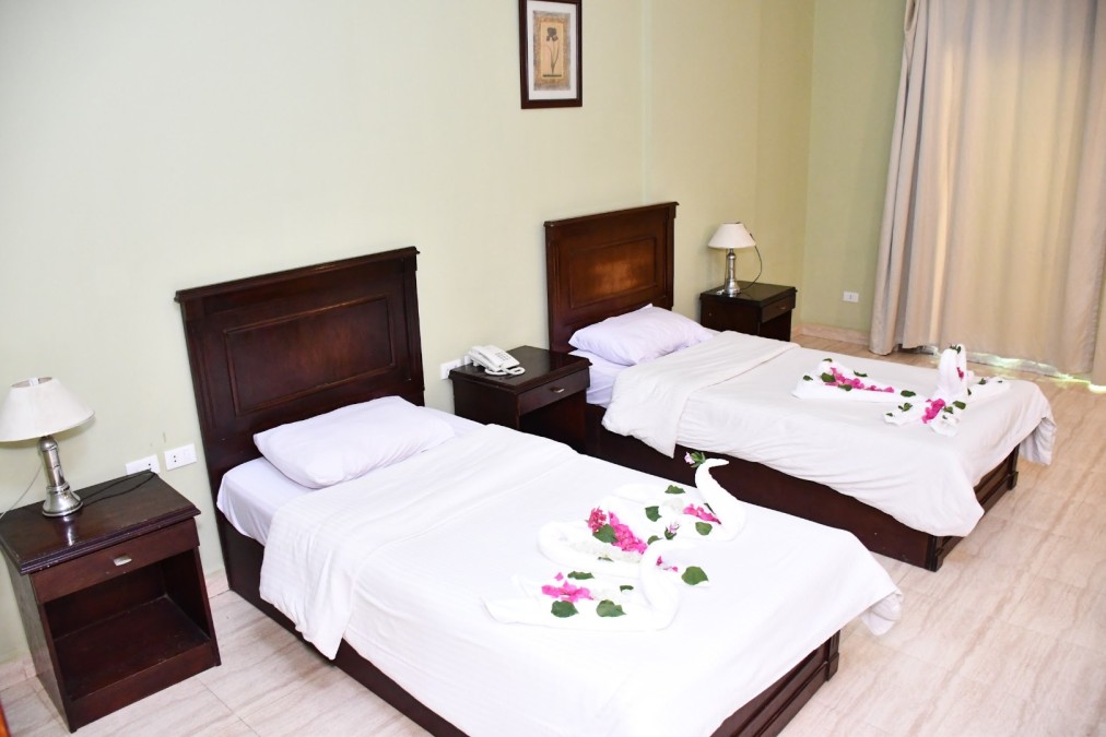 Chambre d'hôtel avec deux lits simples, mobilier en bois et cygnes en serviettes décorés de fleurs