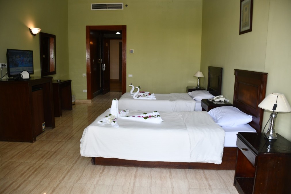 Chambre d'hôtel avec lits jumeaux, murs vert clair et télévision, préparée pour l'hébergement de stage sportif