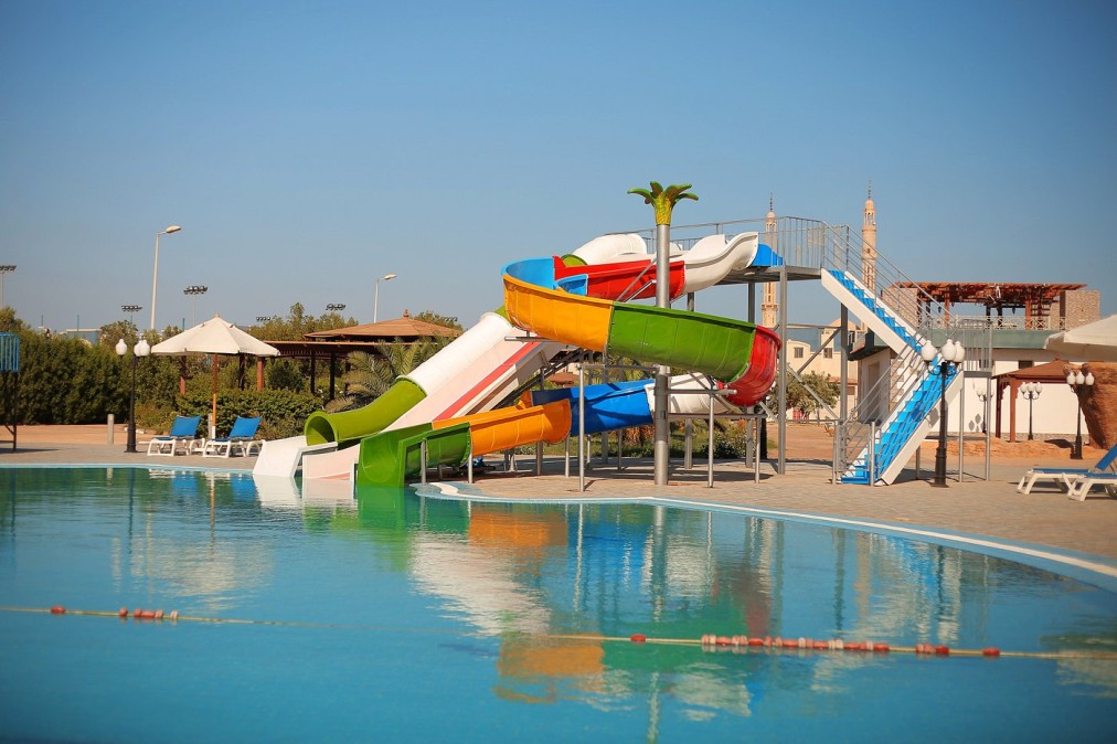 Espace piscine extérieure avec toboggans aquatiques colorés et chaises longues, idéal pour la détente des athlètes après l'entraînement
