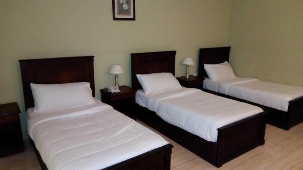 Chambre triple spacieuse avec trois lits simples, têtes de lit en bois et lampes de chevet
