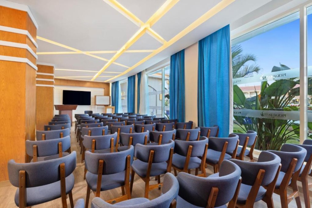 Salle de conférence avec rangées de chaises, écran et paperboard pour les briefings d'équipe.