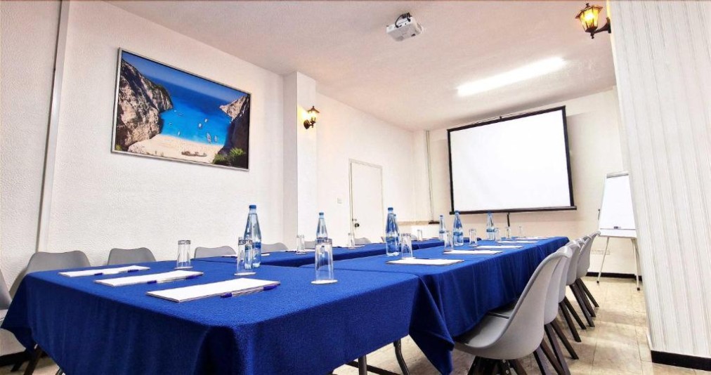 Salle de réunion avec disposition des tables en U, écran de projection et paperboard.